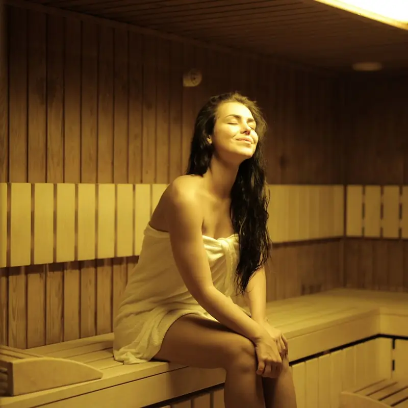 Mulher enrolada em toalha branca em uma sauna de madeira